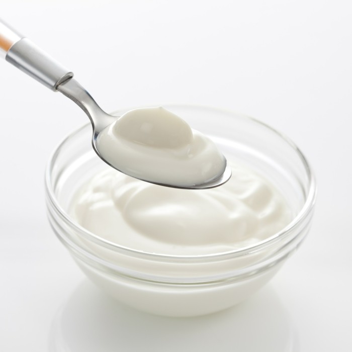 Bowl and spoon with yogurt on white background, close up