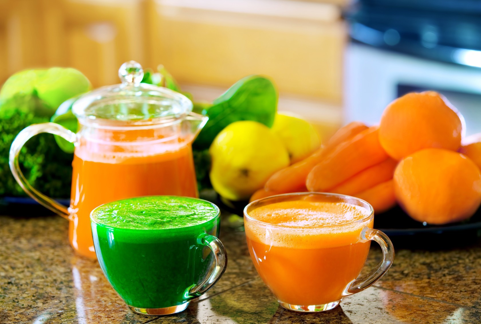 Two cups of fresh vegetable juice on kitchen counter with vegetables in background