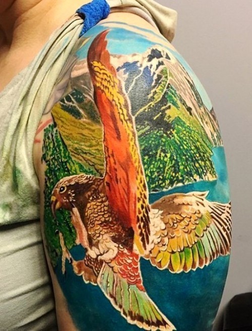 Ideen und Tipps für Ihr erstes oder nächstes Oberarm Tattoo papagei fliegt über bunte landschaft