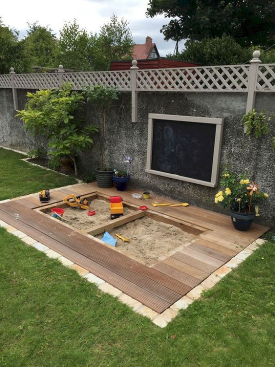 Kinderspielplätze im eigenen Garten Sandkasten sauber halten am Zaun schwarze Kreidetafel Blumen