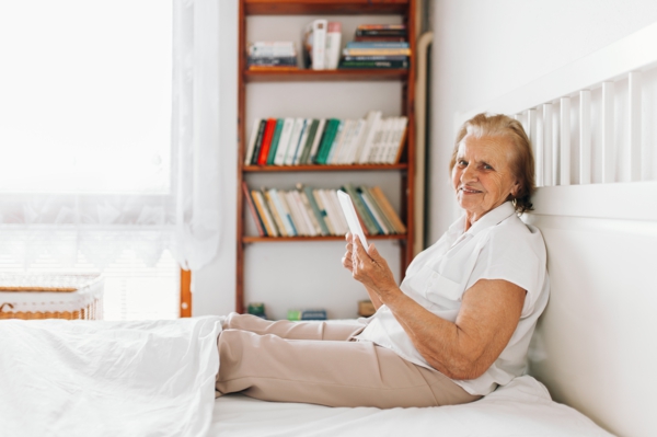 Elderly woman sitting comfortably on bed and using her tablet