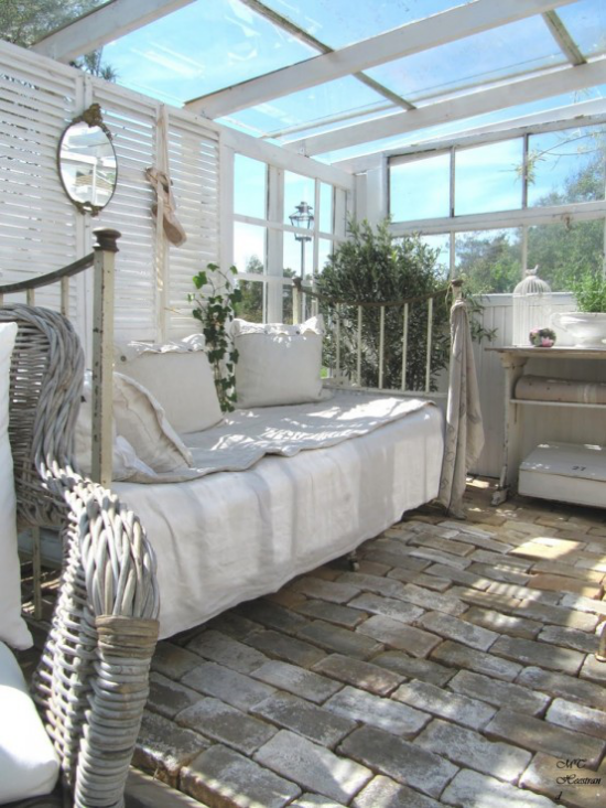 verglaste Veranda Glasveranda Boden mit Steinplatten verlegt bequemes Bett weiße Tagesdecke Korbsessel
