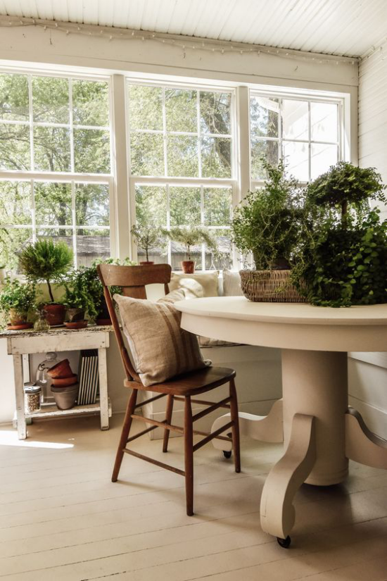 verglaste Veranda Glasveranda runder Tisch in Beige Holzstuhl Kissen viele Grünpflanzen im Raum verteilt