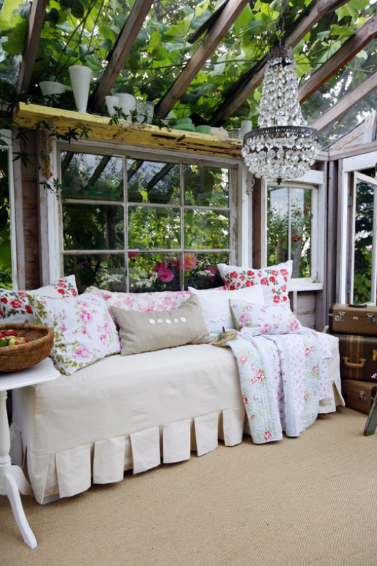 verglaste Veranda Glasveranda sich wie im Garten fühlen viel Grün bequemes Sofa weißer Bezug Blumenmuster in Rosa auf den Deko Kissen Kronleuchter