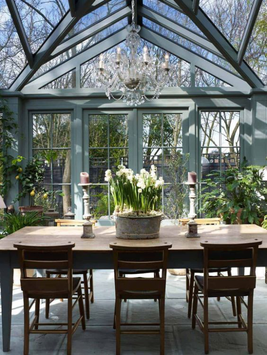 verglaste Veranda geräumige Glasveranda großer Tisch aus dunklem Holz Kübel mit weißen Narzissen Stühle Kronleuchter
