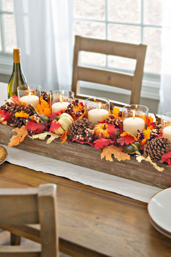 Duftkerzen Herbstdekoration auf dem Esstisch aus Holz rustikal mit bunten Blättern warme Farben kleine Kürbisse Tannenzapfen