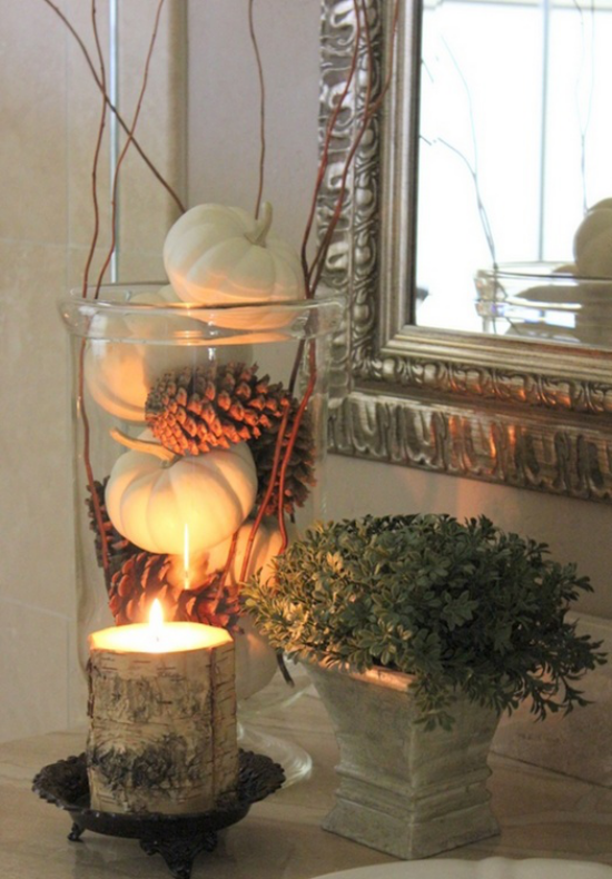 Duftkerzen Herbstdekoration großes Glasgefäß voll mit Kürbissen und Tannenzapfen große Kerze in Baumrinde umwickelt
