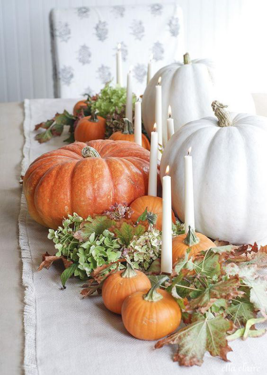 Herbstliche Tischdeko mit Kürbissen weiße und orangefarbene Kürbisse verschiedene Größe Kerzen grüne Blätter
