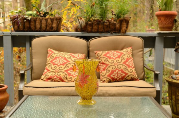Herbstdeko für draußen gepolsterter Zweisitzer Tisch Glasplatte Vase Blumenkästen im Hintergrund
